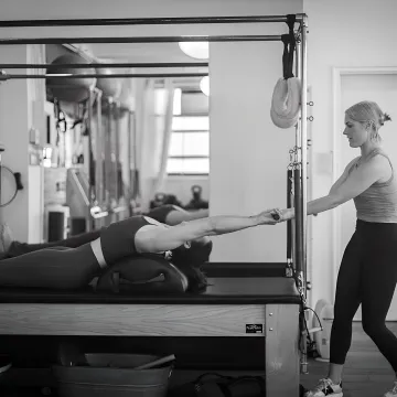 Instructor guiding intermediate reformer Pilates technique