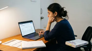 Student researching Oxford college options on laptop with university reference materials