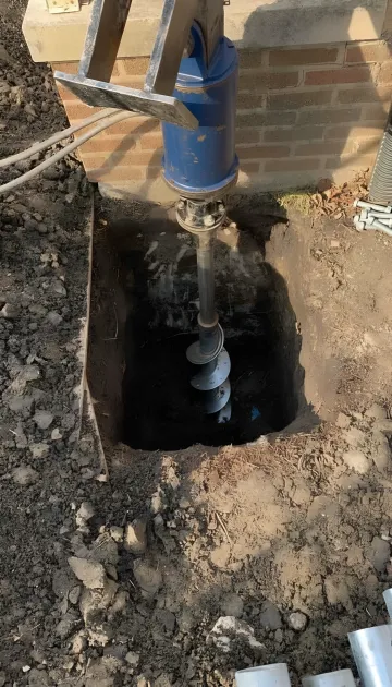 Commercial foundation repair crew installing helical piles on industrial site