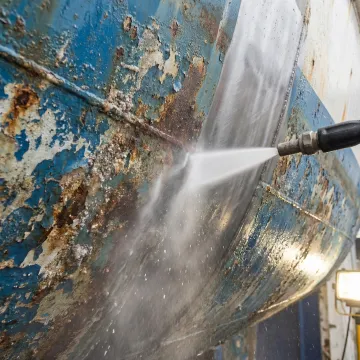 Dustless blasting equipment removing corrosion from boat surface in marine environment
