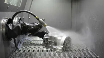 Industrial wet abrasive blasting equipment processing metal component in workshop