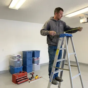 Installer measuring garage ceiling for overhead storage racks