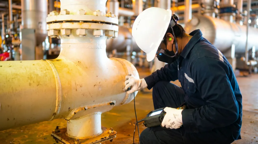 Ultrasonic testing technician inspecting industrial pipe wall thickness on-site