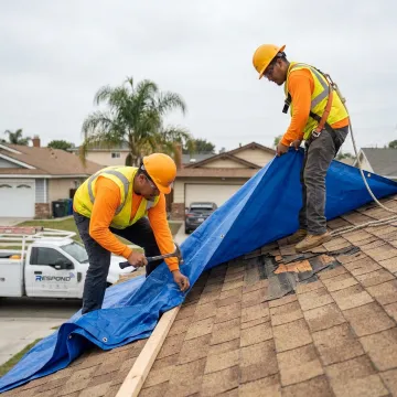 Technicians securing an emergency tarp on a storm-damaged roof