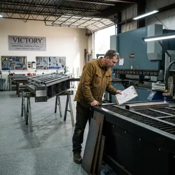 Fabricator reviewing drawings near metalworking equipment