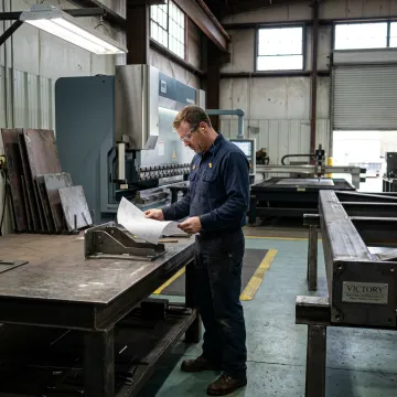 Fabricator reviewing plans beside formed steel parts