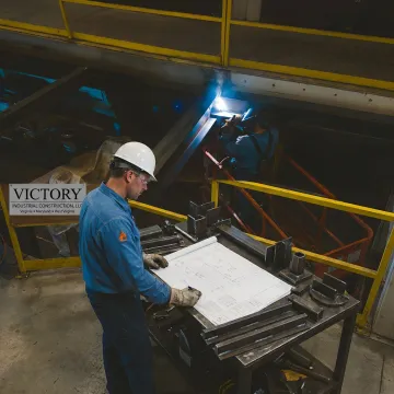 Engineer reviewing CAD drawings beside fabricated metal parts