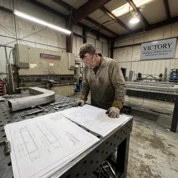 Fabricator reviewing drawings beside finished sheet metal parts