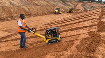 Plate compactor compacting soil fill layers on hillside grading project