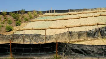 Hillside construction site showing erosion control silt fencing and straw wattles on graded slope