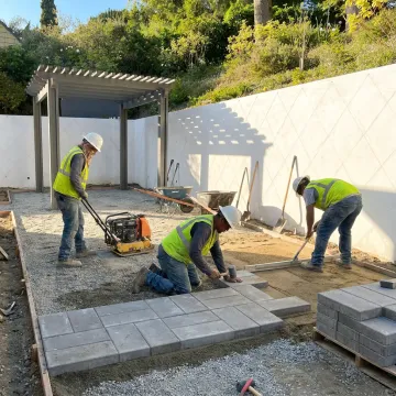 Hardscape crew installing patio pavers on a terraced yard