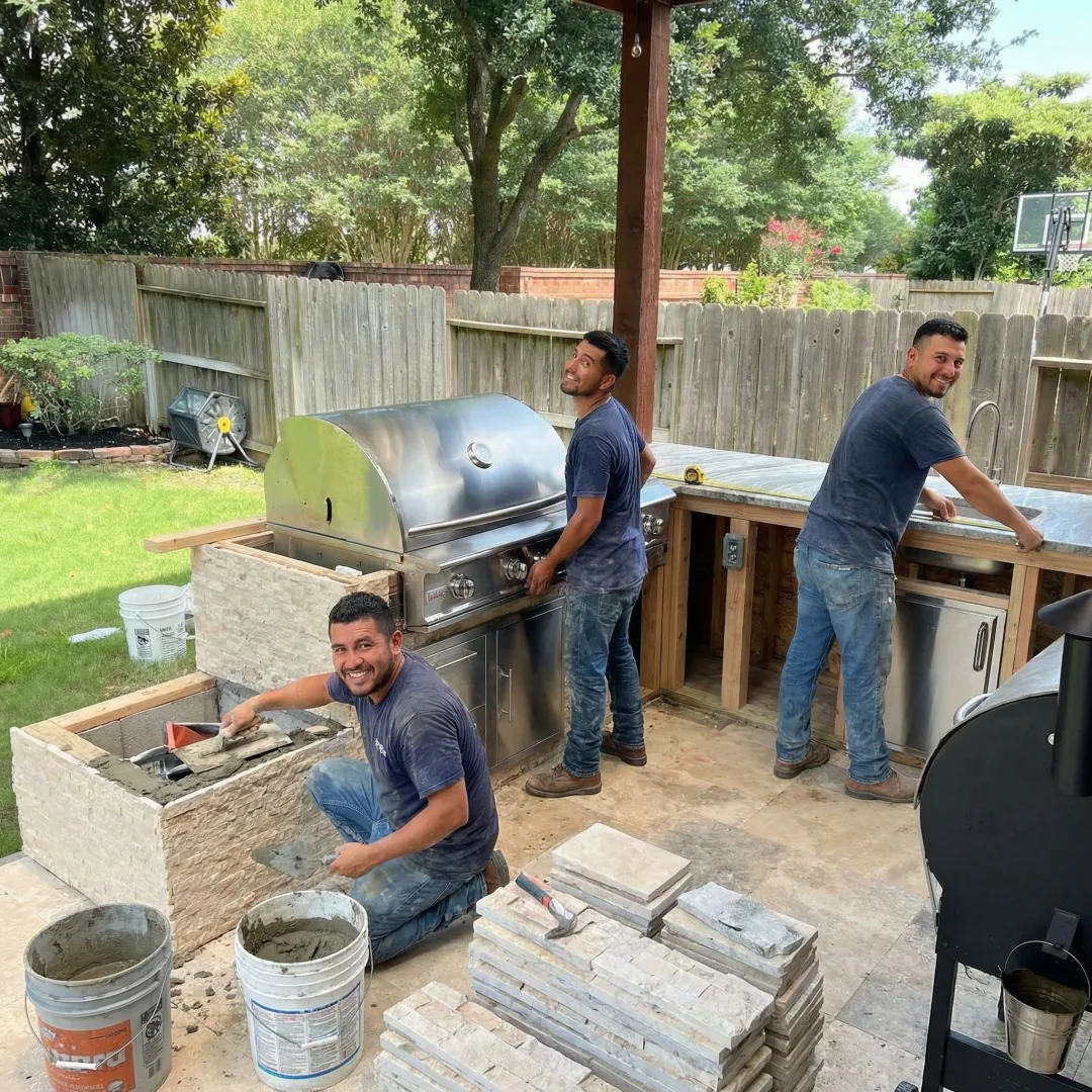 Construction crew installing outdoor kitchen stonework and built-in grill