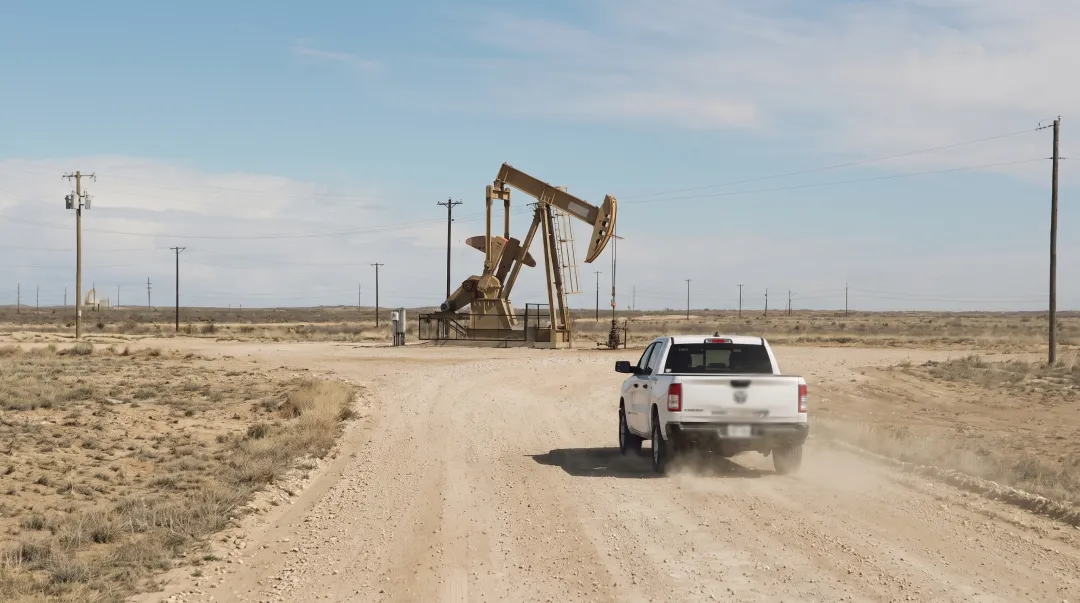 Oil and gas field worker driving on remote rural road to wellsite inspection