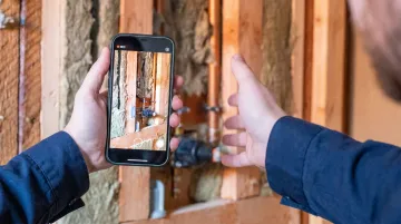 Plumber filming DIY tutorial video on smartphone at residential job site