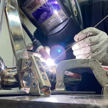 Professional welder performing precision stainless steel welding with sparks and protective equipment