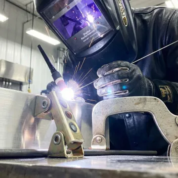 Professional welder performing precision aluminum welding with bright arc and sparks