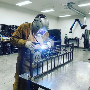 Artisan welding custom wrought iron railing with detailed scrollwork