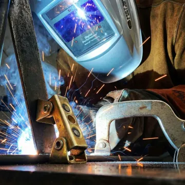 Professional welder in protective gear working with sparks flying from metal welding project