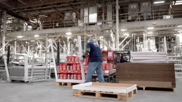 Manufacturing worker performing manual palletizing on production floor with heavy cases